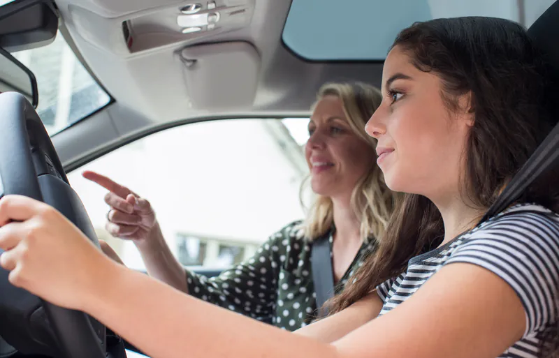 Rij-instructrice wijst haar leerling de weg tijdens een rijles in de lesauto