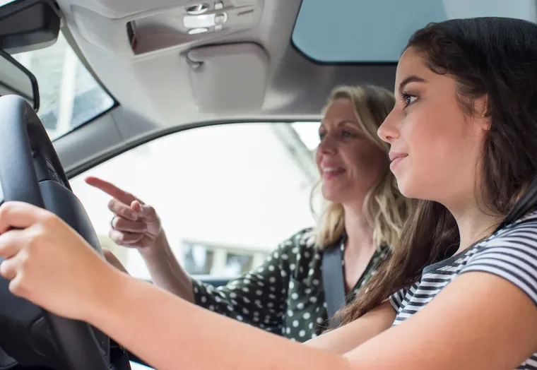 Leerling met de handen aan het stuur van de lesauto terwijl de instructrice de weg wijst: rijscholen vergelijken