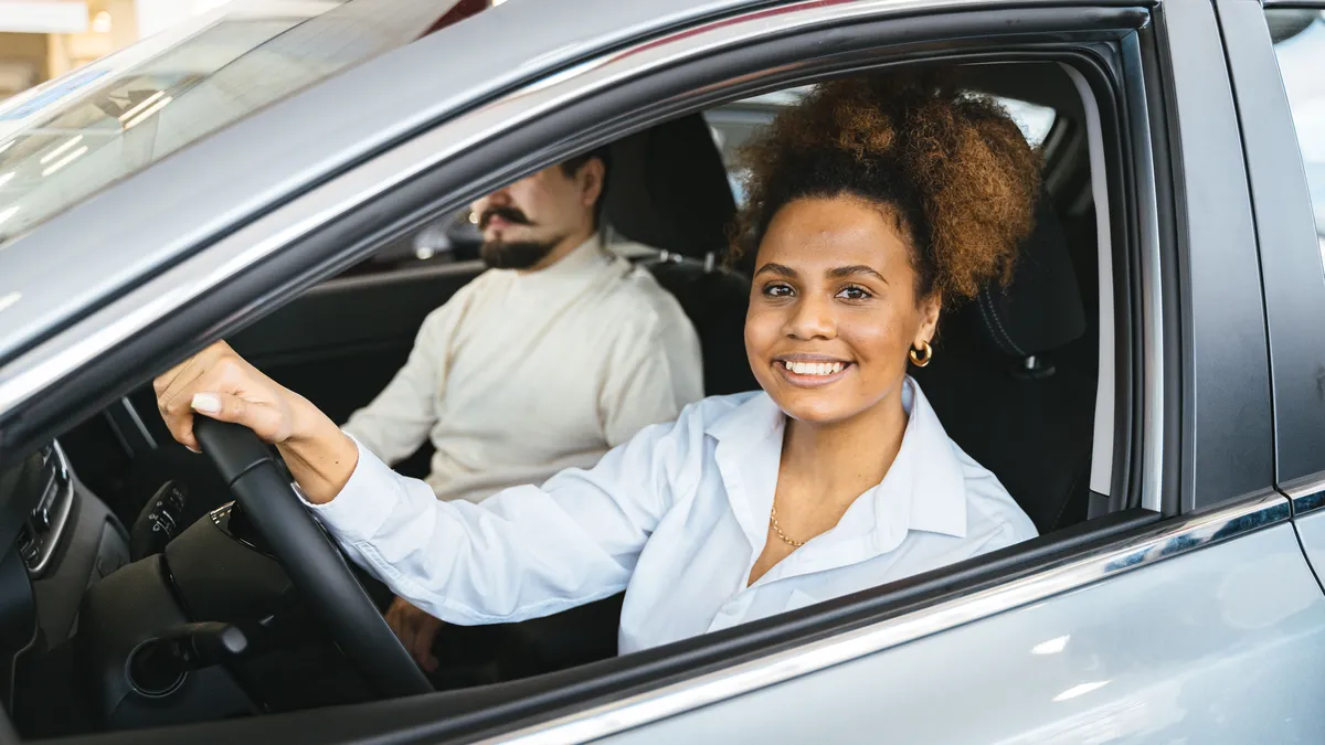 Lachende jonge vrouw achter het stuur van een auto met een man naast haar op de passagiersstoel