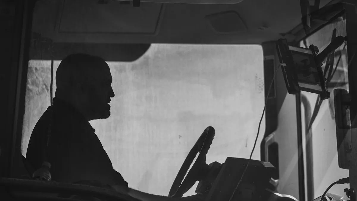 Zwart-witfoto van een vrachtwagenchauffeur achter het stuur in de cabine