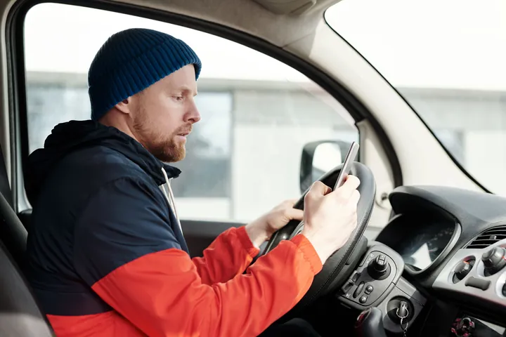 Verkeersboete voor telefoon achter het stuur: man kijkt op zijn telefoon in de auto